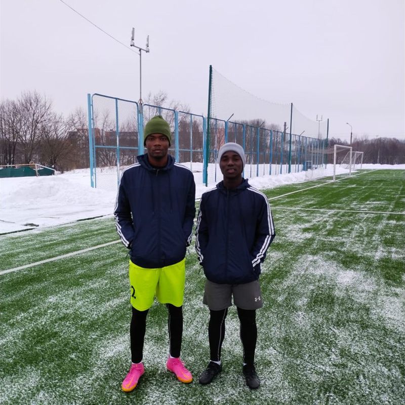 Two young players in tracksuits standing on a snow-covered pitch