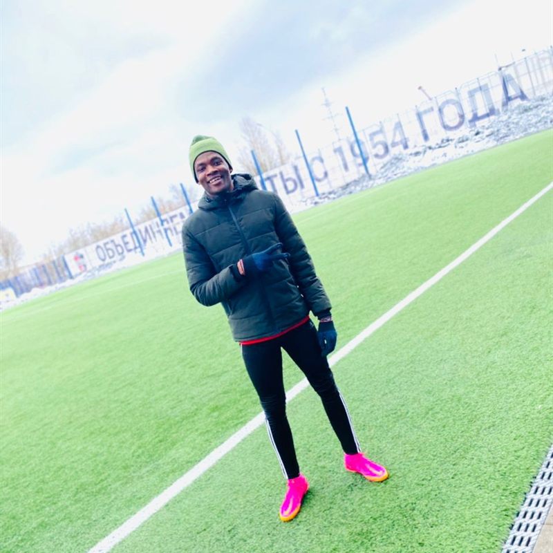 A young player in a winter hat and coat smiling on a floodlit pitch