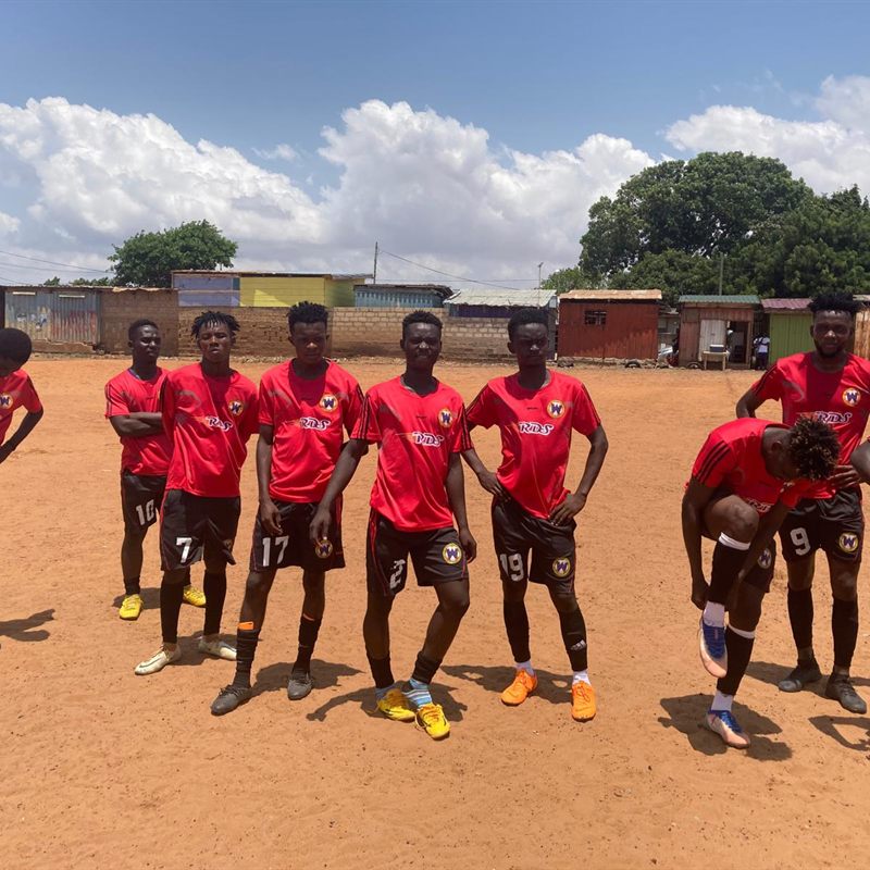 A youth team in red kit lined up on a dirt pitch