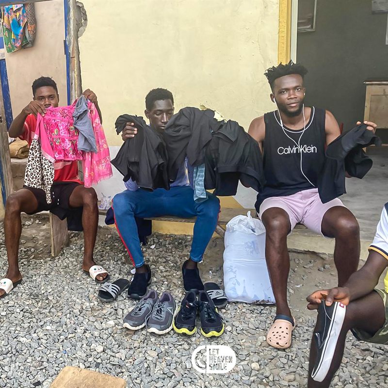 Young men holding up donated clothing and shoes laid out on the ground