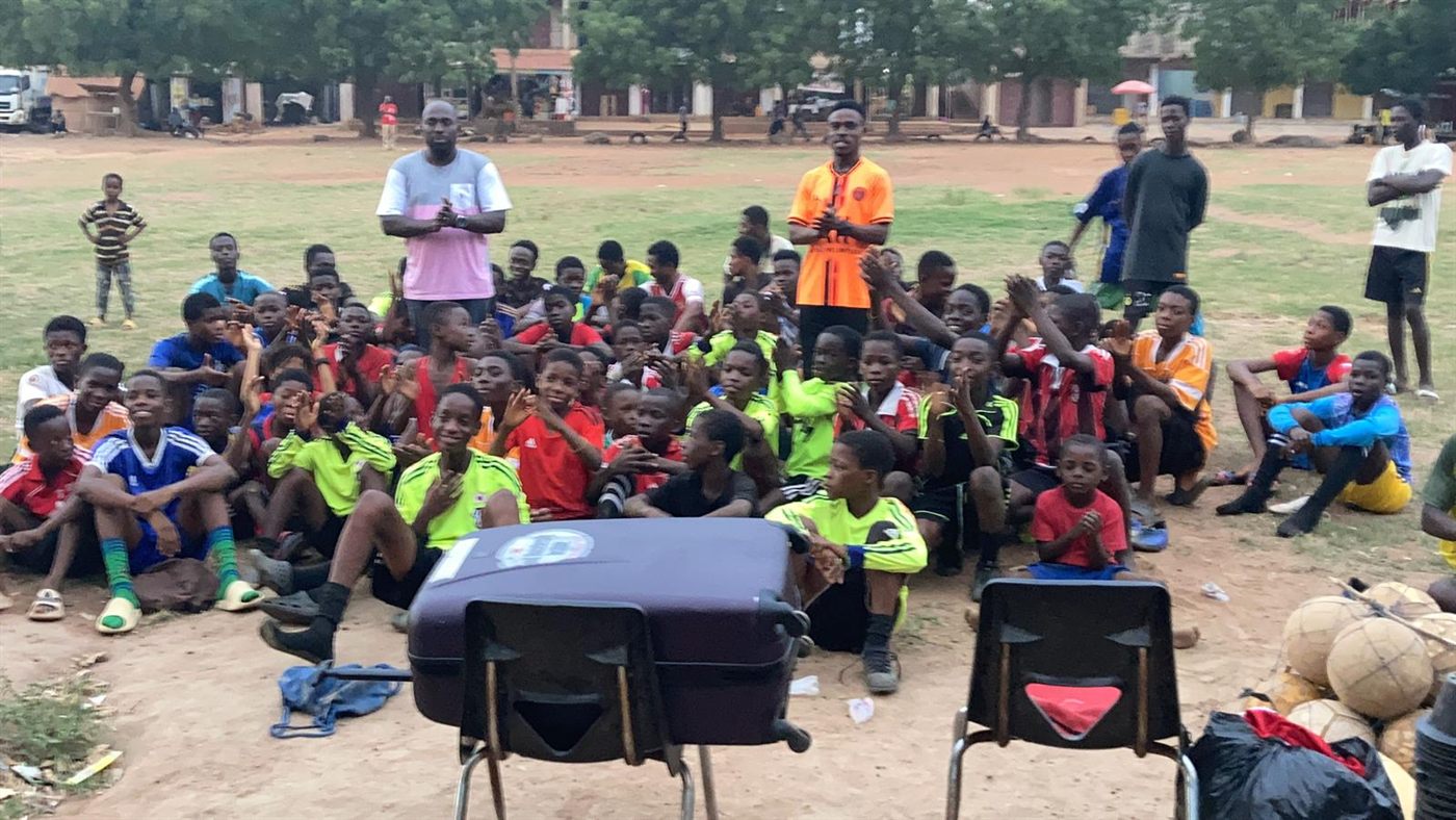 A large group of children seated on the field with their coaches