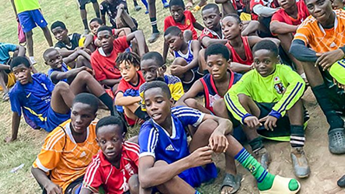 Young players gathered on a grass pitch in Ghana