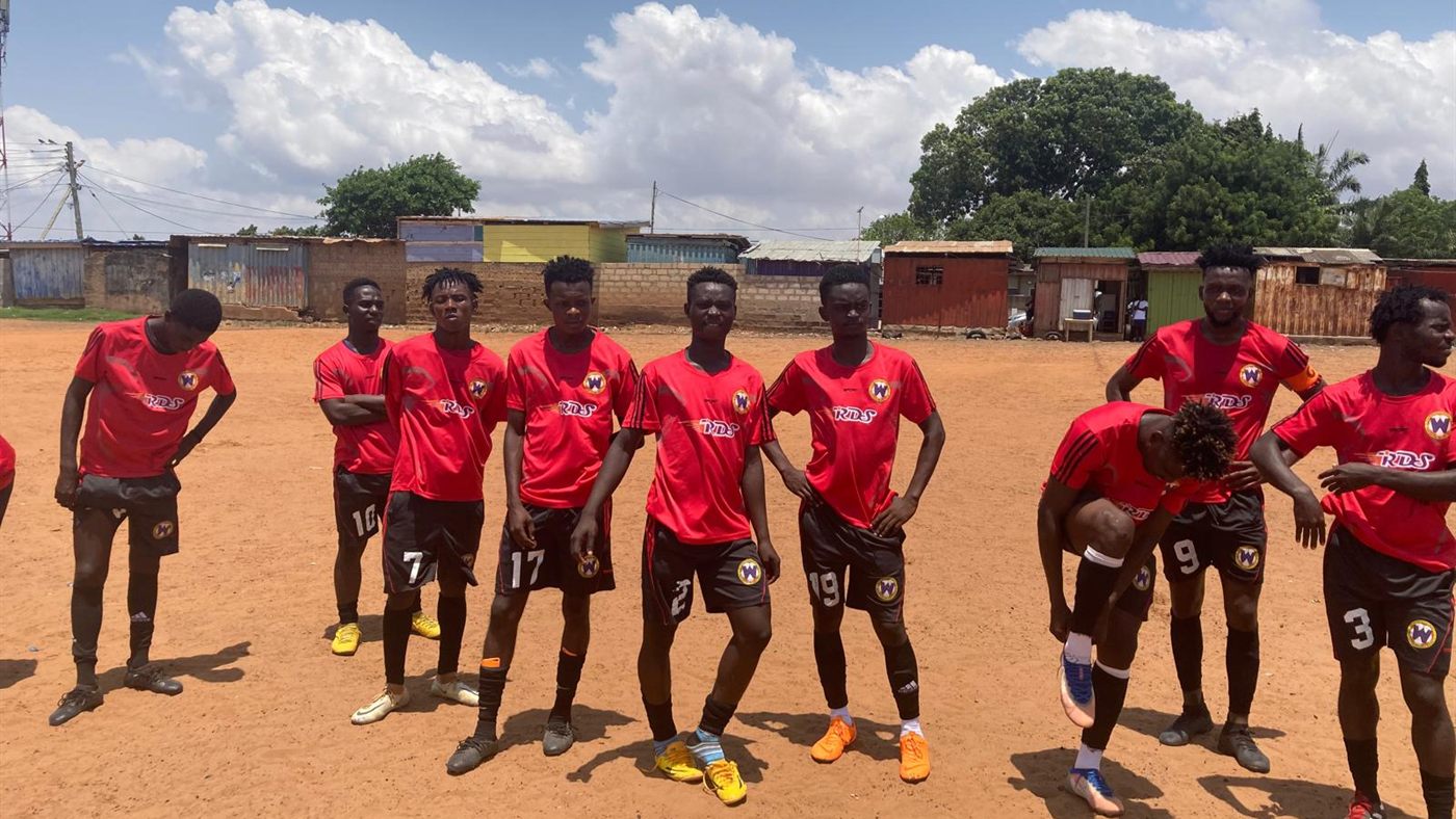 A youth team in red kit on a dirt pitch in a Ghanaian township